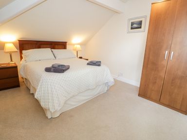 A bedroom with a double bed two bedside tables with lamps a wardrobe and a framed picture on the wall at The Nook in Benllech