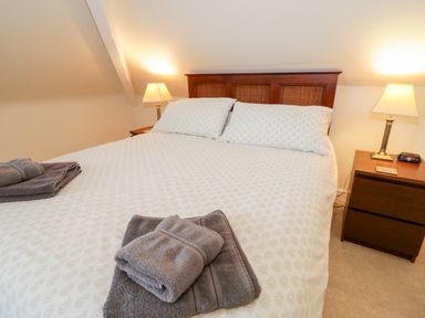 A bedroom with a double bed two bedside tables two lamps and folded towels at The Nook in Benllech