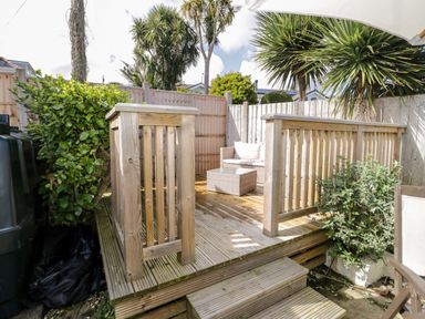 A wooden deck with railings steps a sofa and a coffee table surrounded by plants