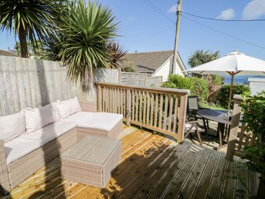 An outdoor patio with a cushioned wicker sofa and table next to wooden railing and a round table with chairs and umbrella at The Nook in Benllech