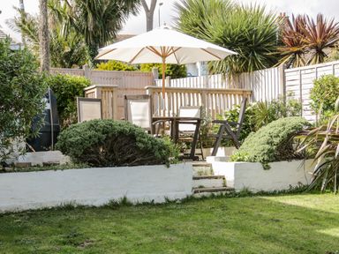 A garden patio with a table umbrella and chairs surrounded by plants and wooden fence at The Nook in Benllech