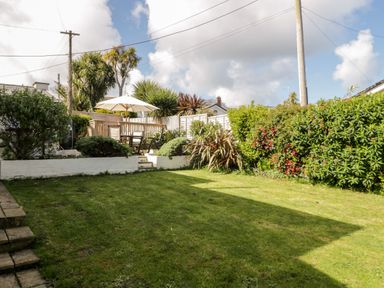 A garden with a lawn seating area with an umbrella and surrounding bushes at The Nook in Benllech