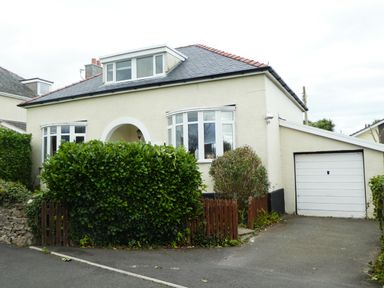A detached house with a driveway garage and front garden with shrubs at The Nook in Benllech