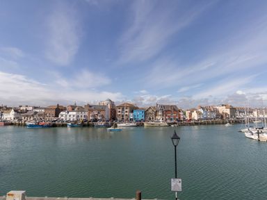 A harbor with boats docked along the waterfront and buildings in the background at Harbourside Cottage in Brewers Quay Harbour