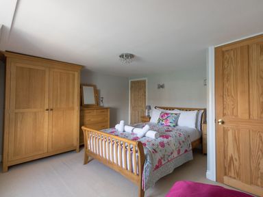 A bedroom with a wooden bed, floral bedding, wooden wardrobe, chest of drawers, and a wooden door at Harbourside Cottage in Brewers Quay Harbour