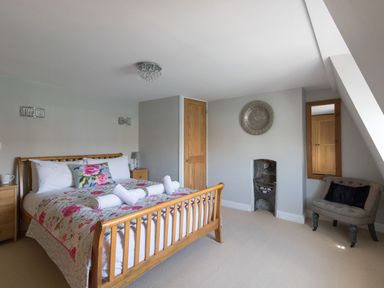 A bedroom with a wooden bed floral bedding rolled towels bedside tables a small armchair and a wall decoration at Harbourside Cottage in Brewers Quay Harbour