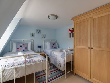 A bedroom with two single beds a wooden wardrobe and a small rug on the floor at Harbourside Cottage Brewers Quay Harbour