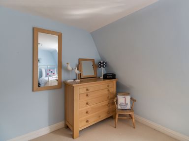 A wooden dresser with a mirror lamp and decorative birds next to a wooden chair with a cushion in a blue painted room at Harbourside Cottage Brewers Quay Harbour