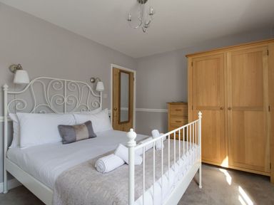 A bedroom with a white metal bed frame wooden wardrobe and chest of drawers at Harbourside Cottage in Brewers Quay Harbour