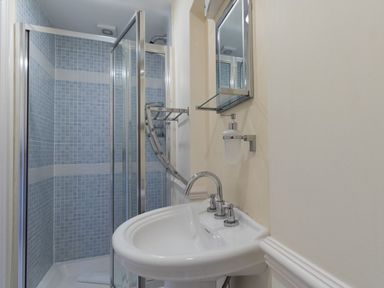 A bathroom with a white sink and blue tiled shower enclosure at Harbourside Cottage Brewers Quay Harbour