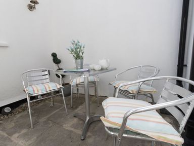 A small outdoor seating area with metal chairs and a table with a teapot and cups at Harbourside Cottage in Brewers Quay Harbour