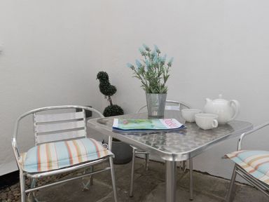 A metal table with a plant, a magazine, a teapot, and two cups surrounded by metal chairs with striped cushions at Harbourside Cottage in Brewers Quay Harbour