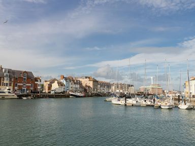 A harbor with boats docked near buildings and a partly cloudy sky at Harbourside Cottage in Brewers Quay Harbour