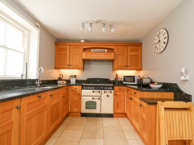 A kitchen with wooden cabinets black countertops a stove a microwave and a clock on the wall at Harbourside Cottage in Brewers Quay Harbour