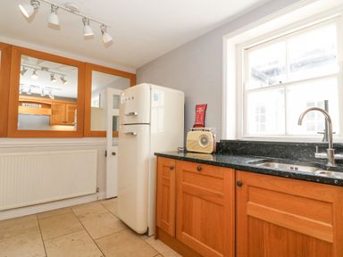A kitchen with wooden cabinets a white fridge a radio on the counter and a window above the sink at Harbourside Cottage Brewers Quay Harbour