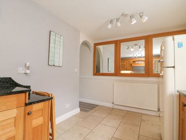 A kitchen with wooden cabinets black countertops a fridge a radiator and a large three-panel mirror on the wall at Harbourside Cottage Brewers Quay Harbour