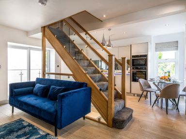 An open living space with a blue sofa near carpeted stairs and a kitchen dining area with a glass table and chairs at The Old Sweet Shop in Conwy