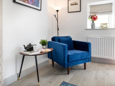 A blue armchair next to a wooden side table with a teapot cup plant and plate of pastries at The Old Sweet Shop in Conwy