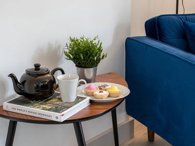 A side table with a black teapot white mug a book potted plant and a plate of pastries next to a blue sofa at The Old Sweet Shop in Conwy