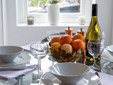 A dining table set with bowls glasses cutlery a bowl of fruit and a bottle of wine at The Old Sweet Shop in Conwy