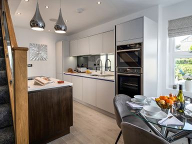A kitchen with an island, built-in ovens, a glass dining table set, and a window at The Old Sweet Shop in Conwy