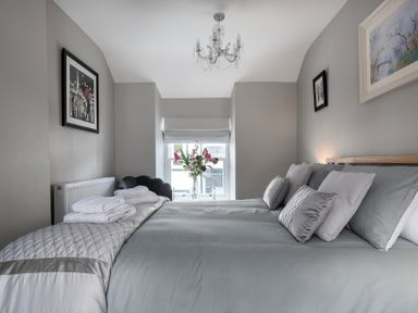 A bedroom with a bed with gray bedding pillows and towels near a window with flowers at The Old Sweet Shop in Conwy