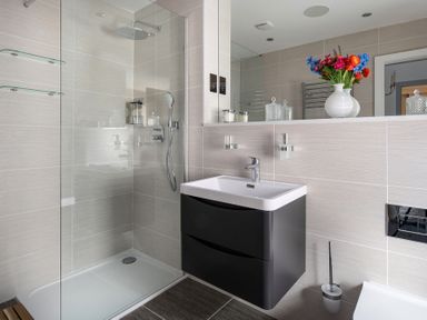 A bathroom with a shower area a black sink vanity with faucet and a vase with flowers on the countertop at The Old Sweet Shop in Conwy