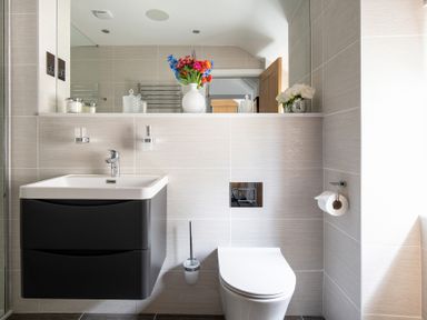 A bathroom with a wall-mounted sink and toilet with flowers on a shelf at The Old Sweet Shop in Conwy