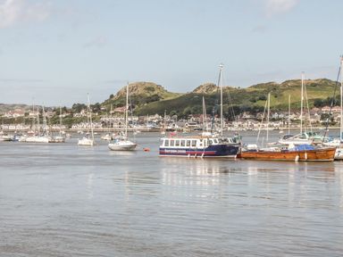 Boats moored on a river with houses and hills in the background at The Old Sweet Shop in Conwy