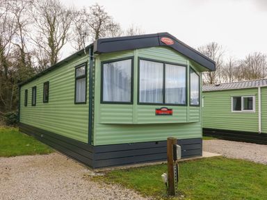 A green static caravan with multiple windows parked on a gravel and grass area at 12A Borwick Lakes in South Lakeland Leisure Village