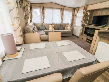 A dining table with placemats and a lamp in front of a sofa and a television in a living area at 12A Borwick Lakes South Lakeland Leisure Village