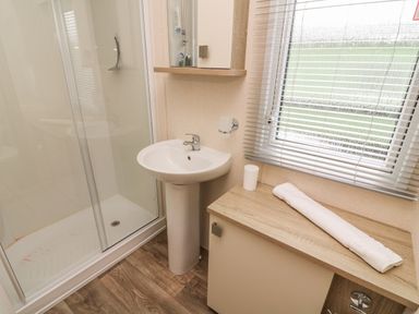 A bathroom with a shower, sink, countertop with a towel and cup near a window with blinds at 12A Borwick Lakes South Lakeland Leisure Village