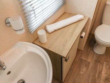 A bathroom with a sink toilet wooden cabinet with a towel and cup on it at 12A Borwick Lakes South Lakeland Leisure Village