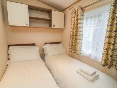 A bedroom with two single beds white bedding folded towels on one bed and a window with patterned curtains at 12A Borwick Lakes in South Lakeland Leisure Village