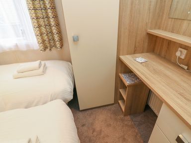 A bedroom with two beds with folded towels a curtain a wooden desk and a wardrobe at 12A Borwick Lakes South Lakeland Leisure Village