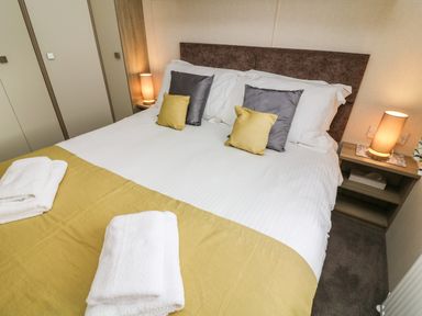 A bedroom with a bed with white and yellow bedding two bedside tables with lamps at 12A Borwick Lakes South Lakeland Leisure Village