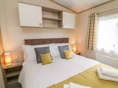 A bedroom with a bed with pillows and folded towels by a window with curtains at 12A Borwick Lakes in South Lakeland Leisure Village