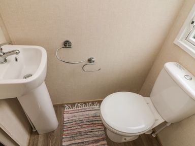 A bathroom with a white sink and toilet and a striped rug on the floor at 12A Borwick Lakes South Lakeland Leisure Village