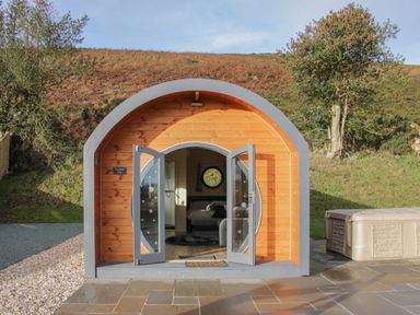 A curved wooden pod with open double doors showing a bed inside and a hot tub outside at Stapeley Pod in White Grit near Chirbury