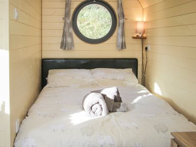 A bedroom with a bed folded towels a round window and a wall lamp at Stapeley Pod in White Grit near Chirbury