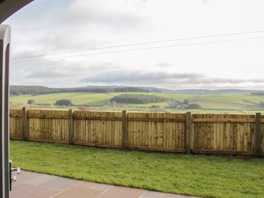 A backyard with grass a wooden fence and rolling hills in the background at Stapeley Pod in White Grit near Chirbury