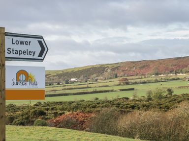A countryside landscape with a road sign for Lower Stapeley and a Sunrise Pods luxury glamping sign in White Grit near Chirbury