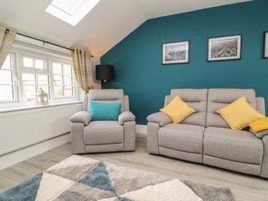 A sitting room with gray armchair and sofa with cushions near a window and teal painted wall with framed pictures at New Inn Apartment in Tholthorpe near Easingwold