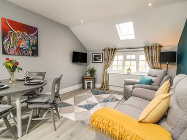 A living room with a gray dining table and chairs a colorful painting and a gray sofa with yellow cushions at New Inn Apartment in Tholthorpe near Easingwold