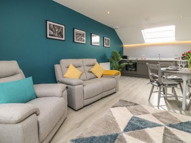 A living room with gray sofas and yellow and blue cushions near a kitchen and dining table at New Inn Apartment in Tholthorpe near Easingwold
