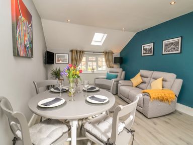 A dining table with four place settings and a vase of flowers in a living room with sofas and cushions at New Inn Apartment in Tholthorpe near Easingwold
