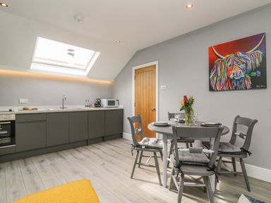 A kitchen and dining area with gray cabinets and chairs a round table with set plates and flowers a colorful painting on the wall at New Inn Apartment in Tholthorpe near Easingwold