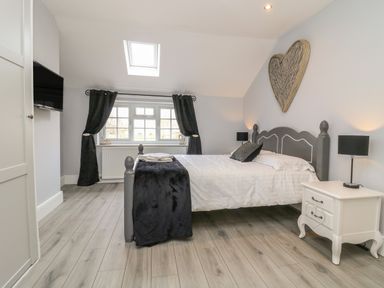 A bedroom with a bed black curtains white bedside table and a wooden heart decoration on the wall at New Inn Apartment in Tholthorpe near Easingwold