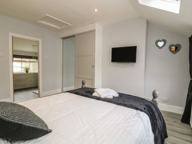 A bedroom with a bed with folded towels on it a wall-mounted TV two heart-shaped wall mirrors and a doorway to a bathroom at New Inn Apartment in Tholthorpe near Easingwold