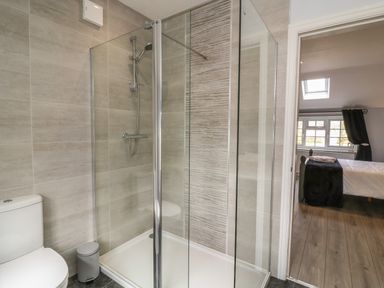A bathroom with a shower enclosure a toilet and a small trash bin next to a bedroom at New Inn Apartment in Tholthorpe near Easingwold